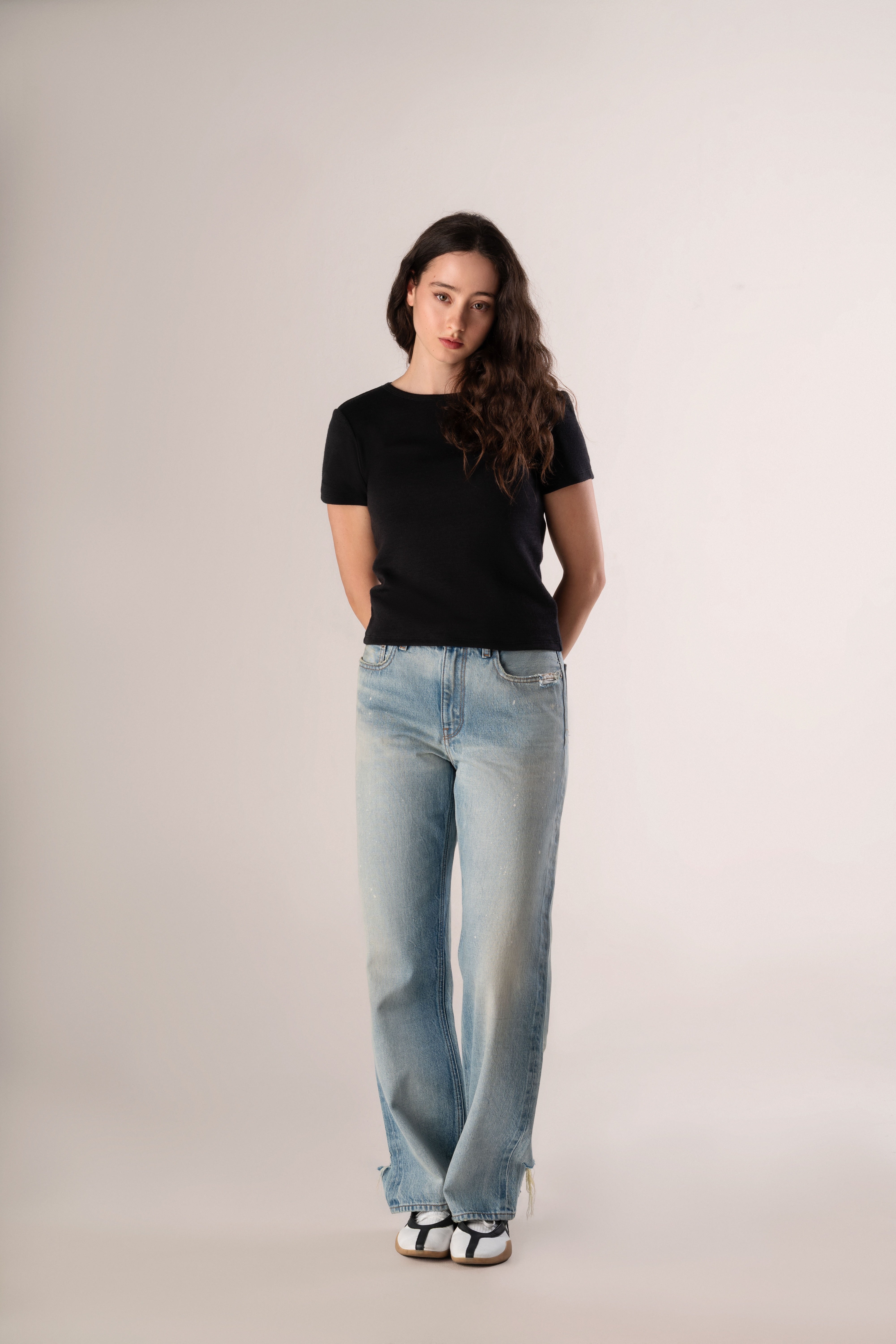 Woman wearing a black t-shirt and light blue jeans on a plain background