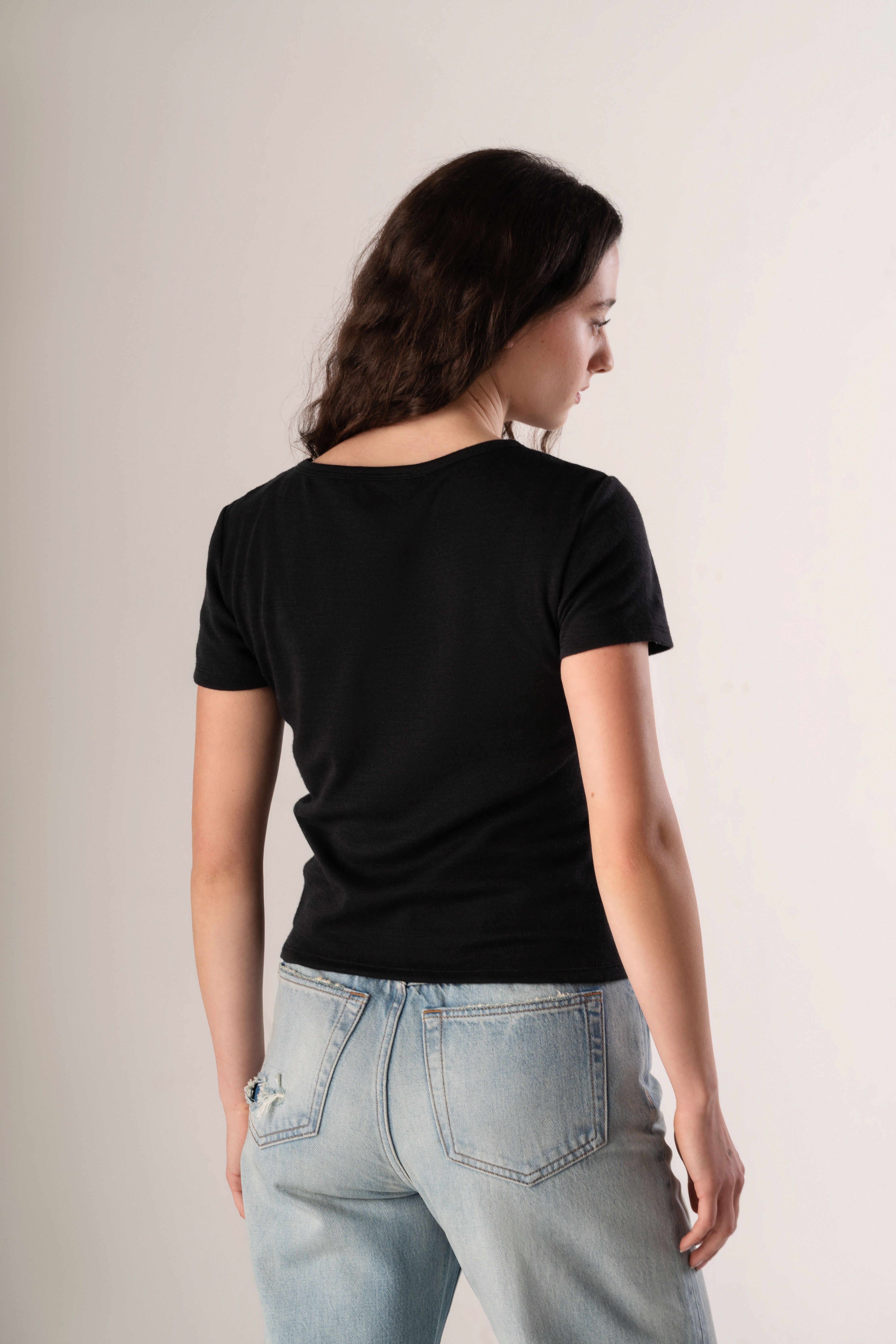 Woman wearing a black t-shirt and light blue jeans against a plain background