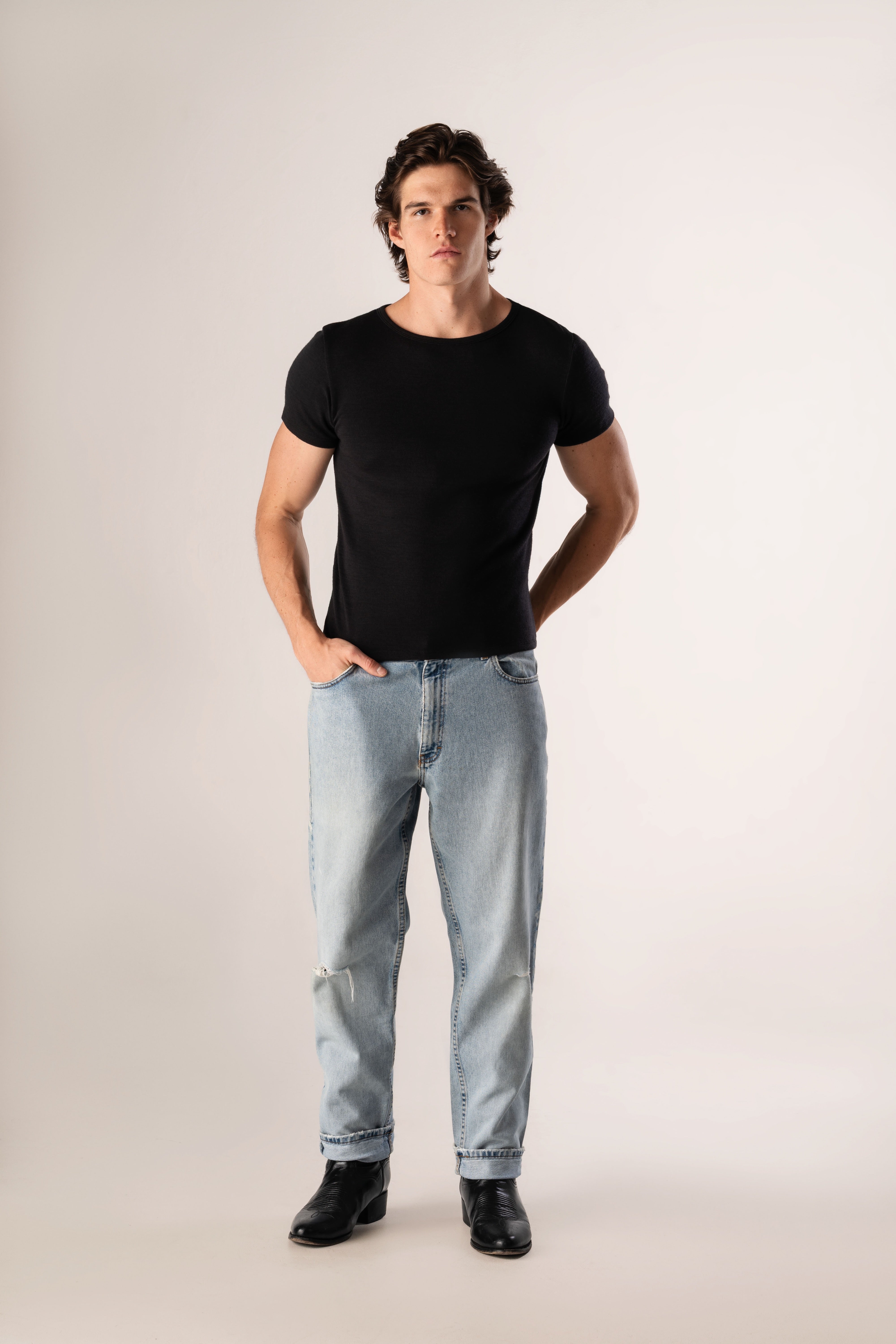 Man wearing a black t-shirt and light blue jeans on a plain background