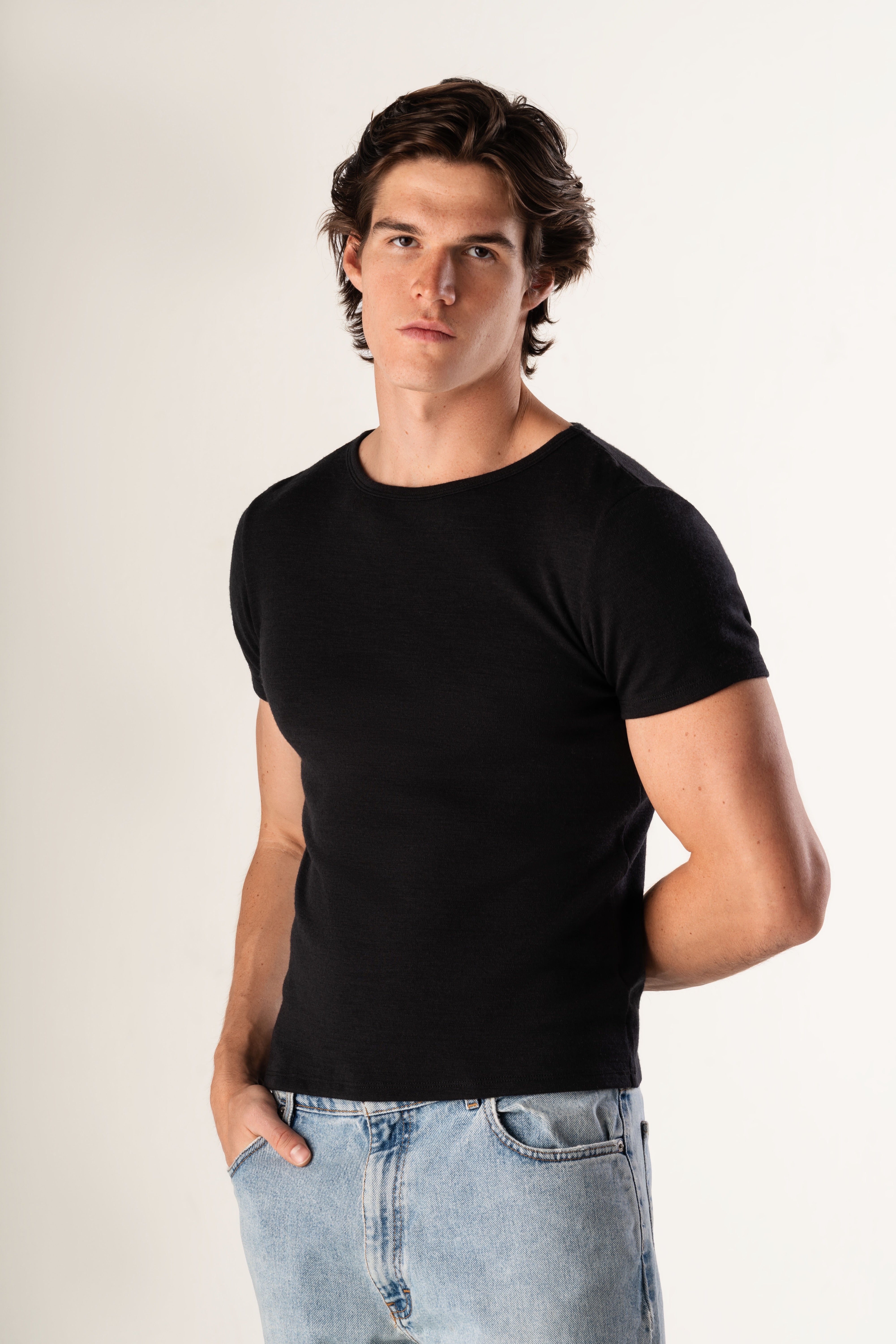 Man wearing a black t-shirt and light blue jeans against a plain background