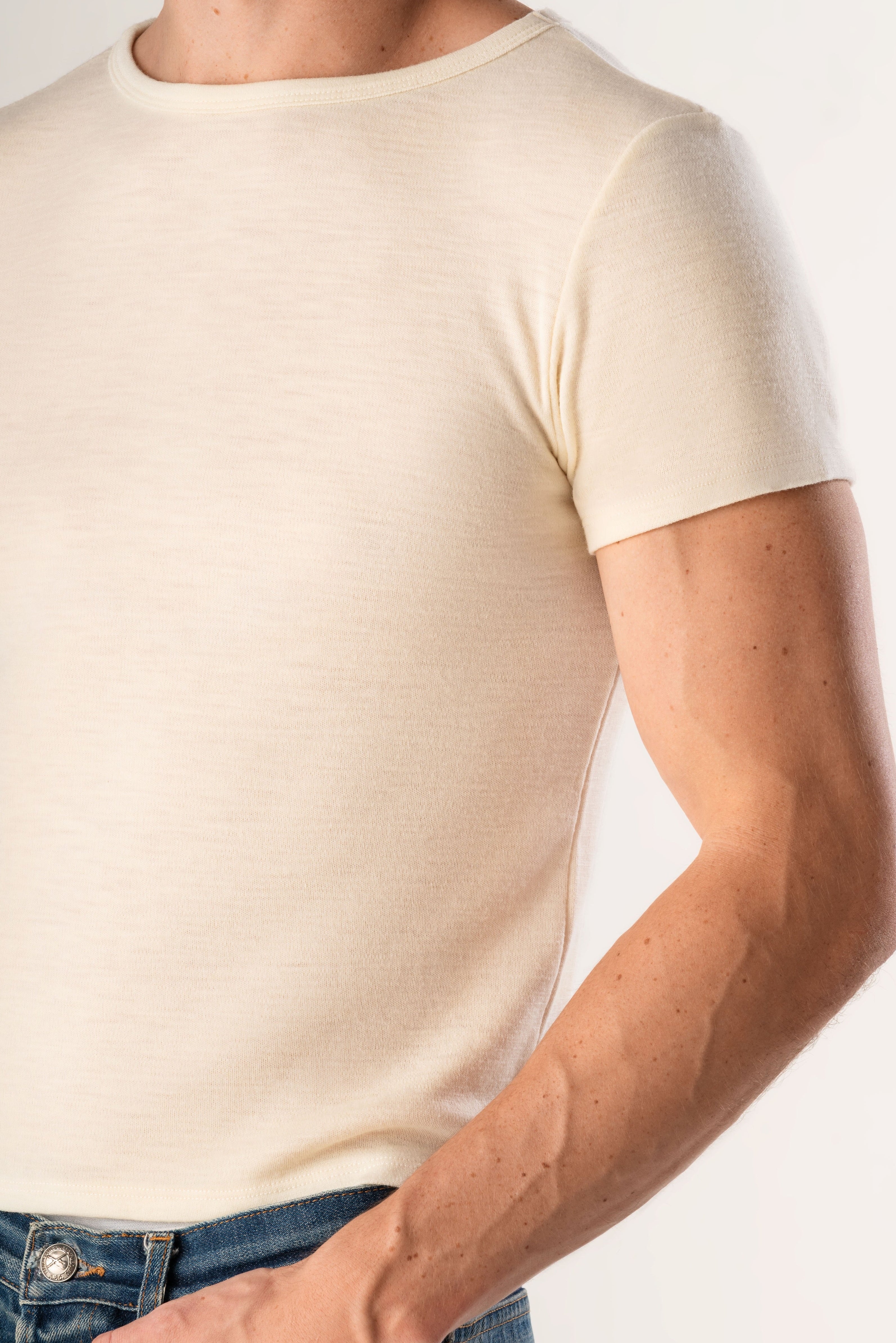 Man wearing a plain white t-shirt and blue jeans on a light gray background