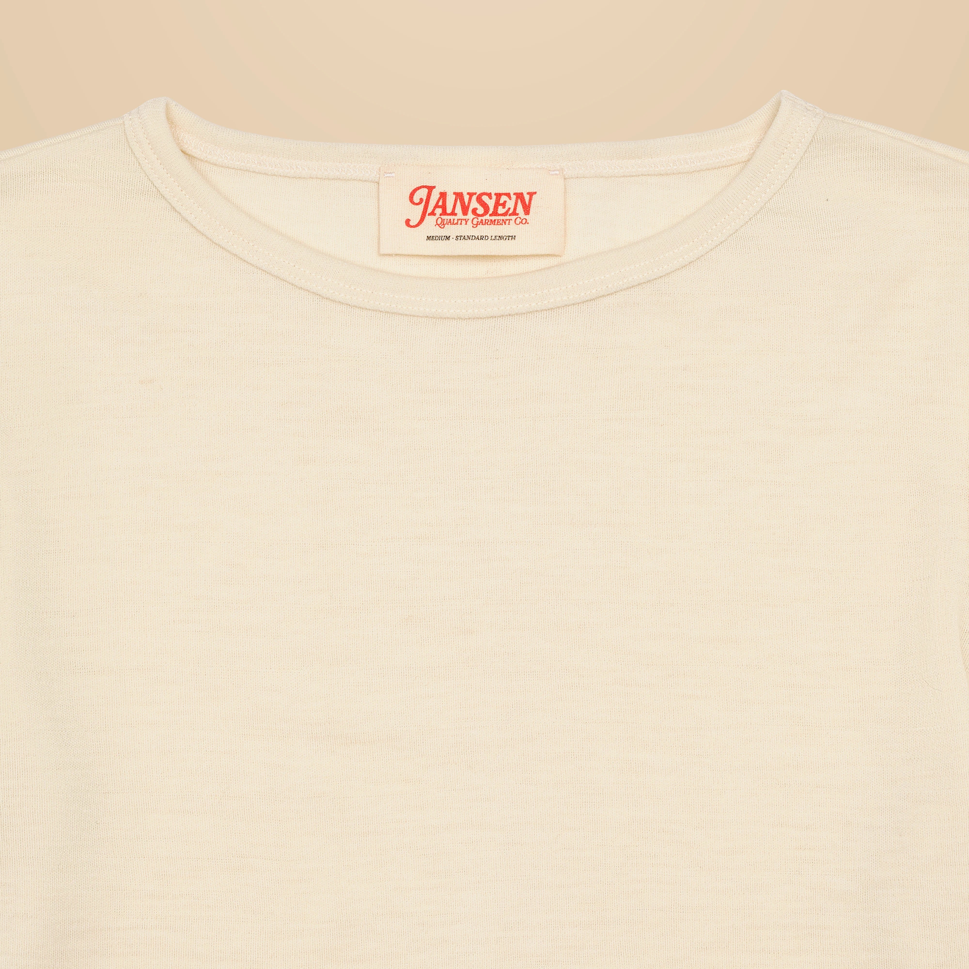 White/Cream merino wool t-shirt with a "Jansen Quality Garment Co." neck label on the inside neck, placed on a beige background.