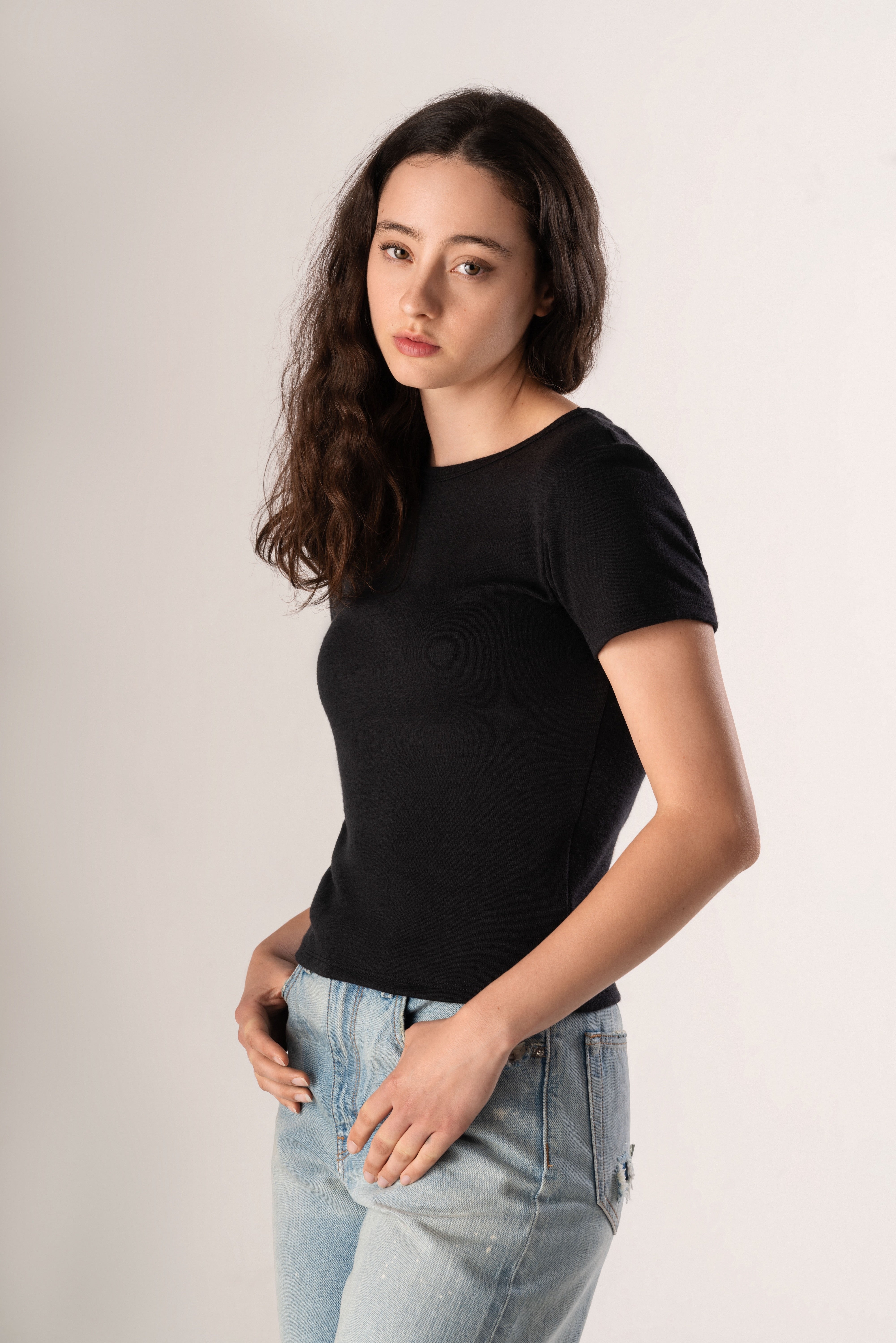 Woman wearing a black t-shirt and light blue jeans against a plain background