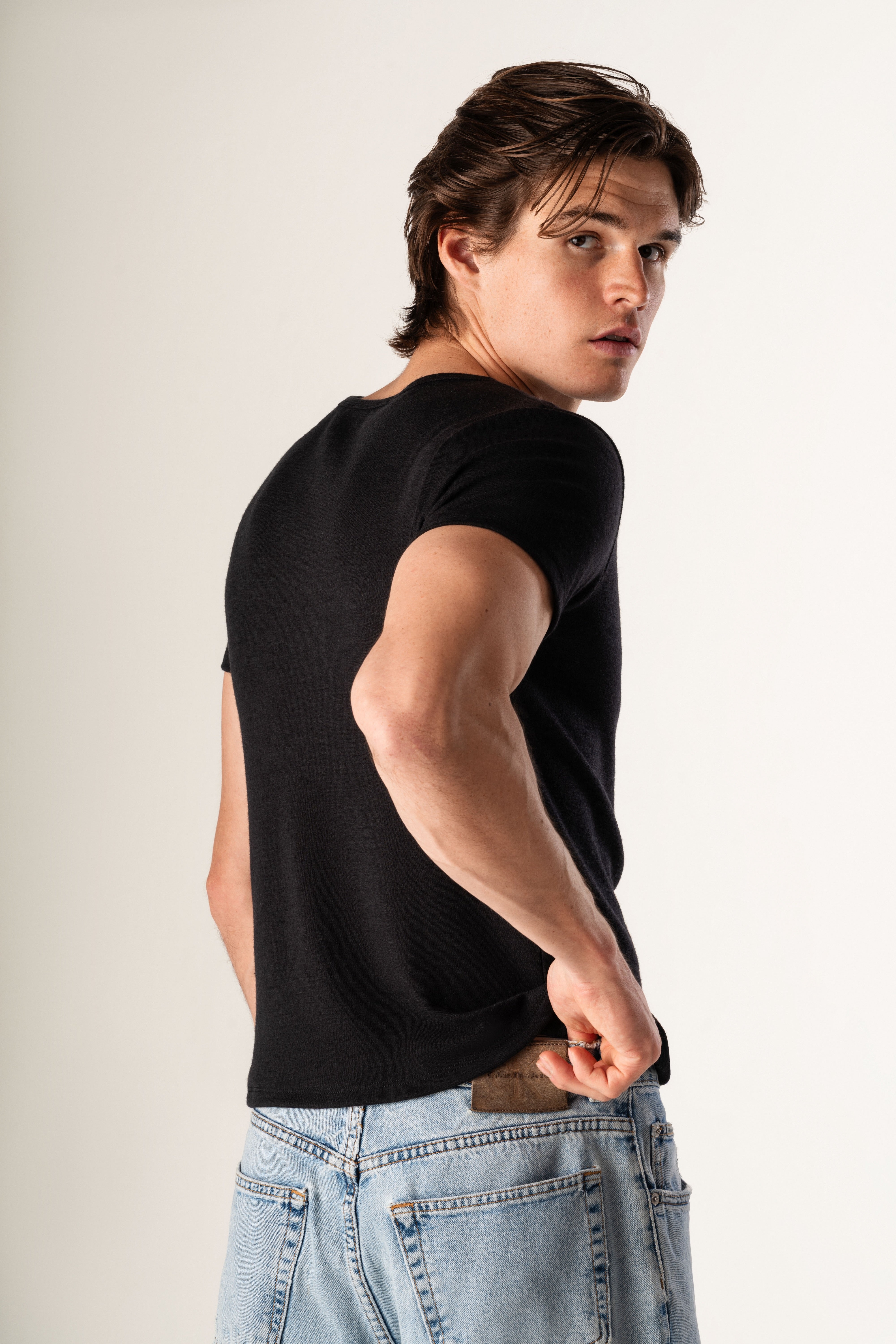 Man wearing a black tee shirt and light blue jeans against a plain background