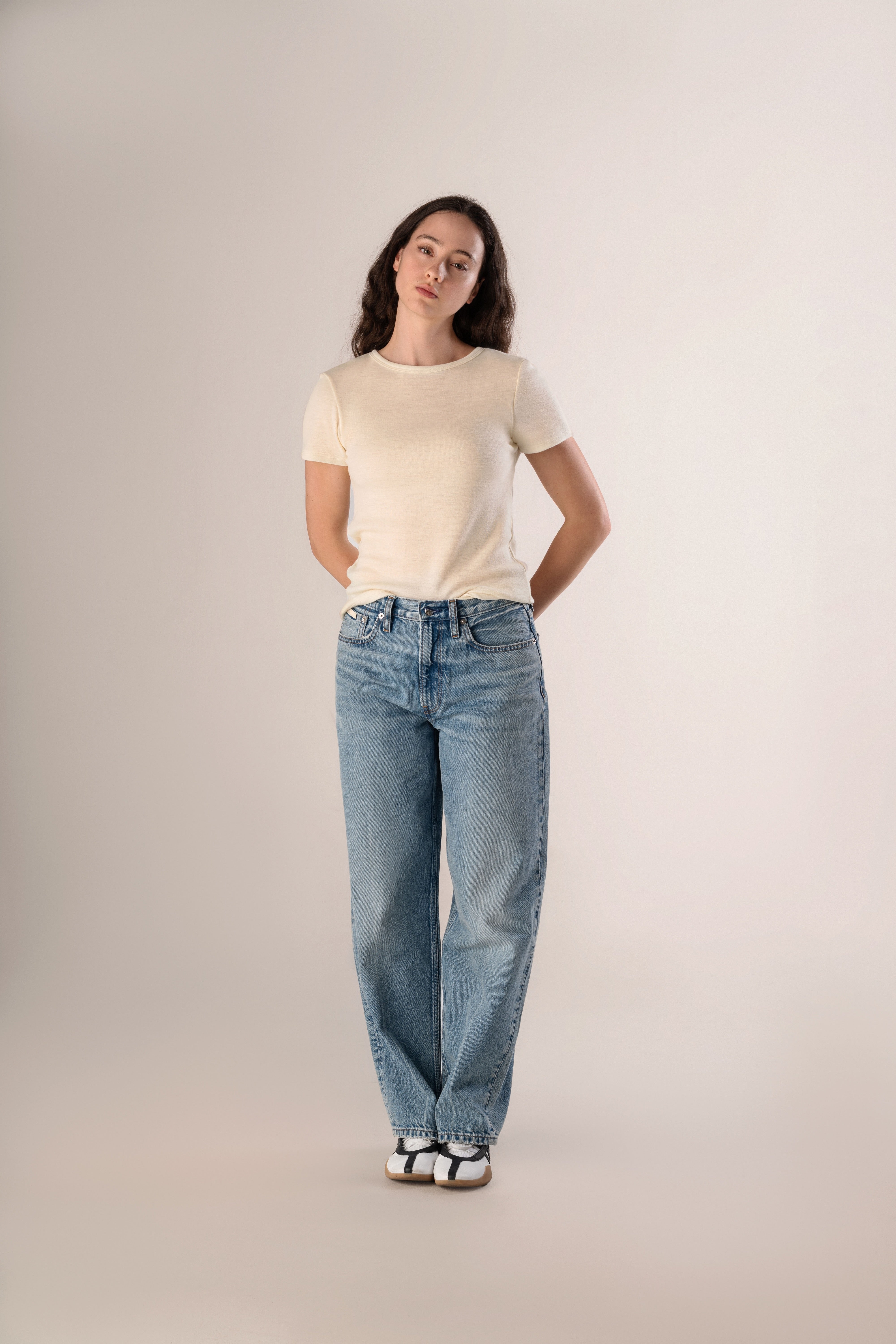 Woman wearing a beige t-shirt and light blue jeans on a plain background