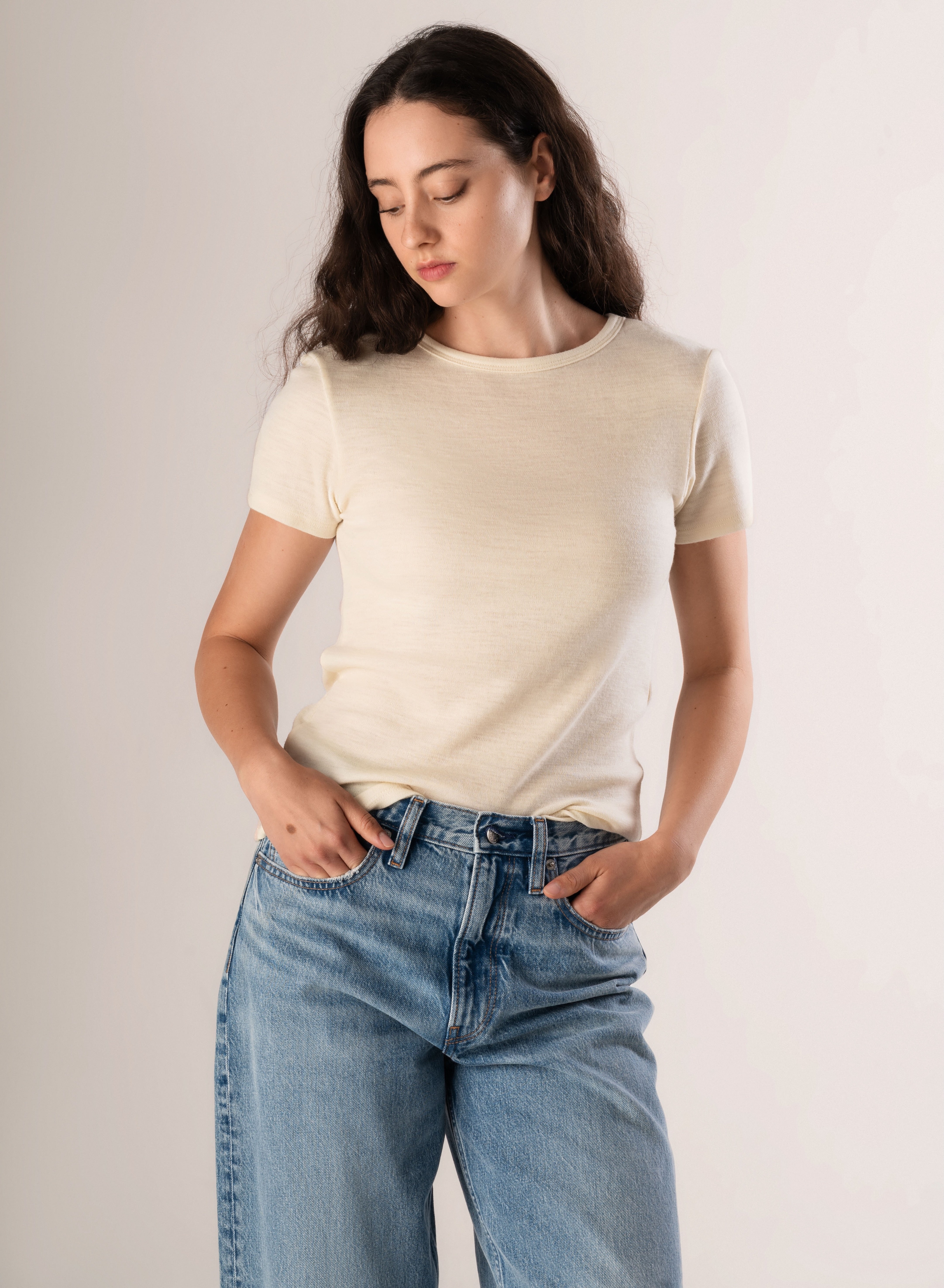 Woman wearing a white/cream t-shirt and blue jeans against a plain background