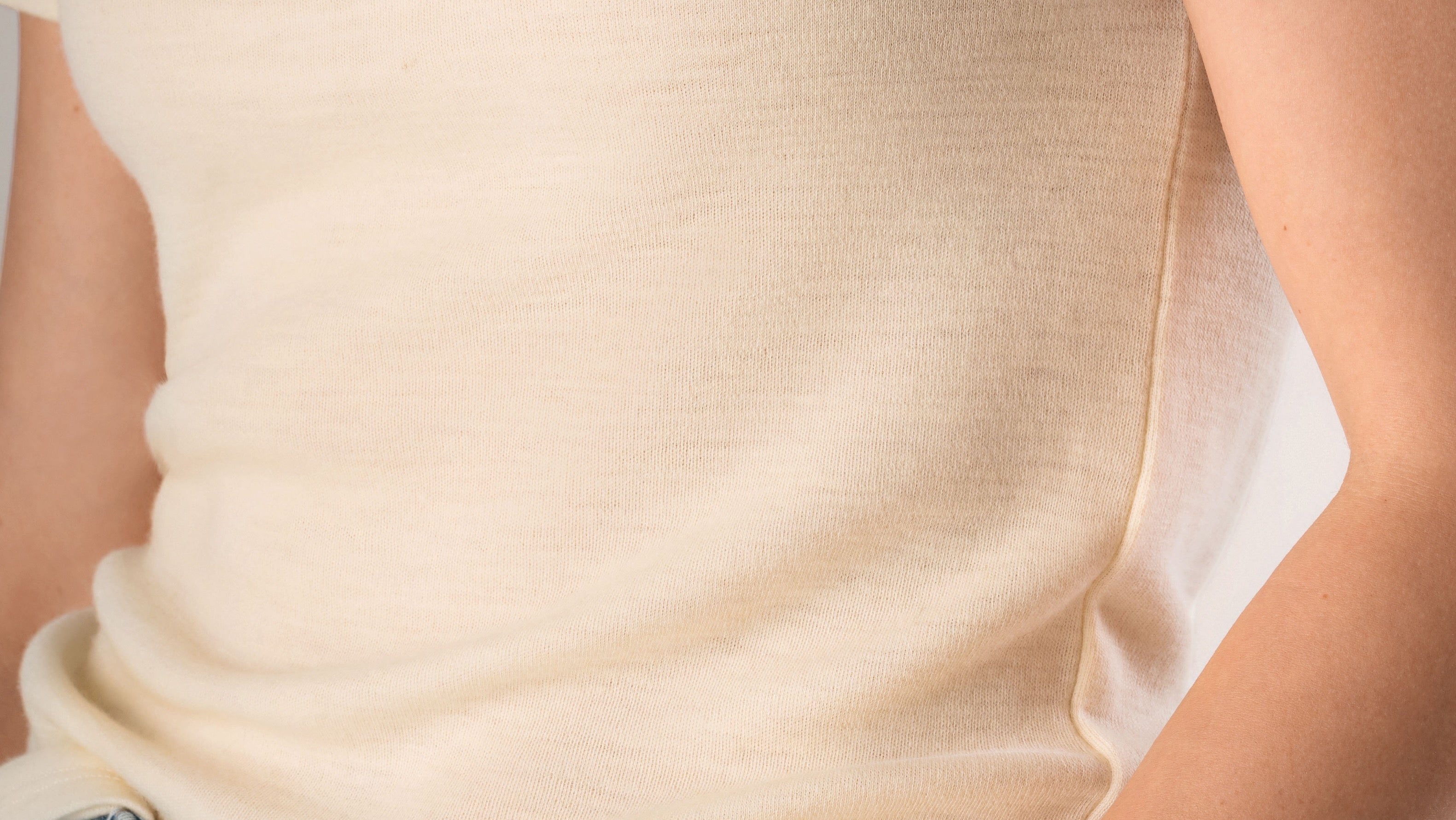 Person wearing a cream-colored t-shirt and blue jeans on a white background