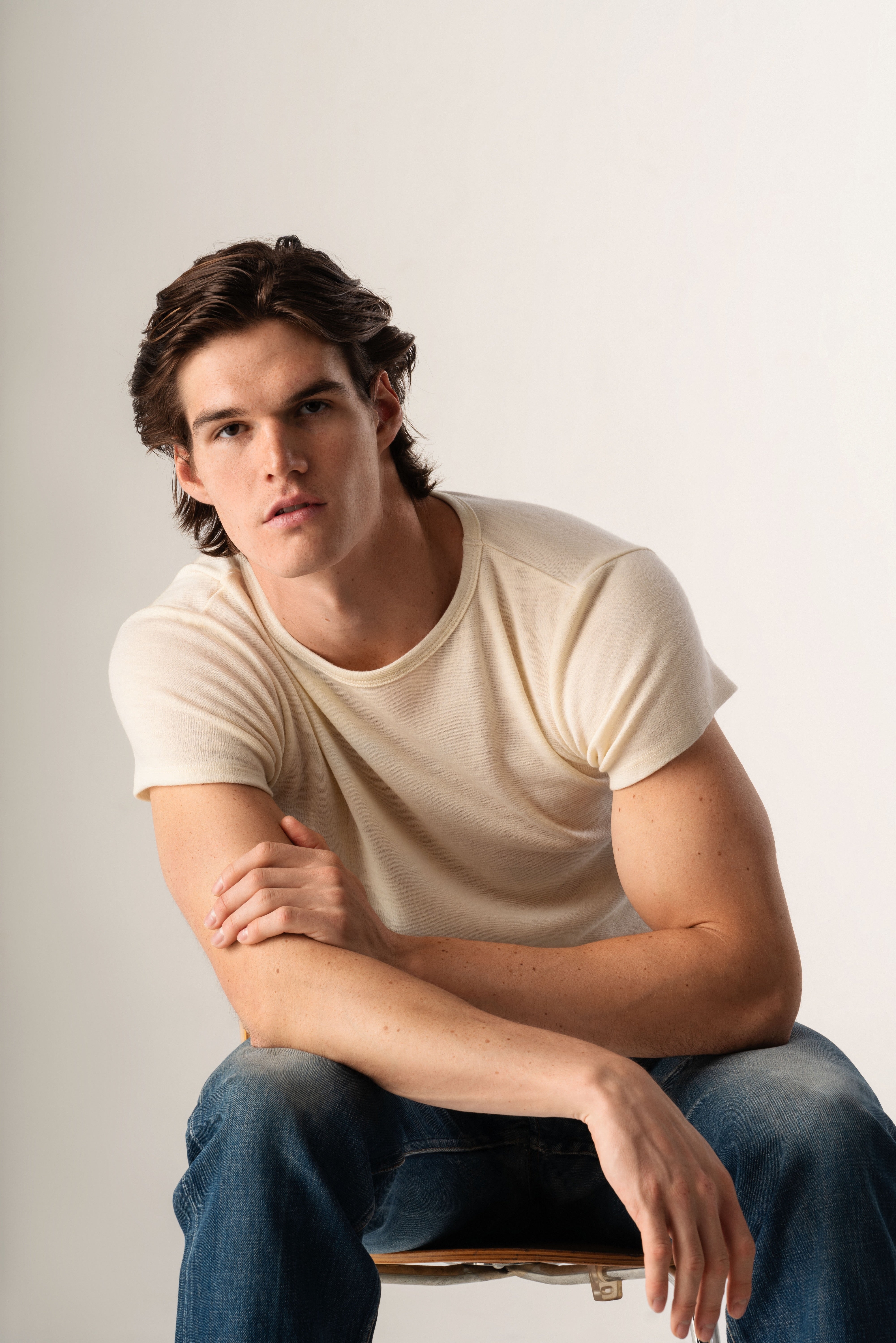 Man wearing a white t-shirt and blue jeans sitting on a white background
