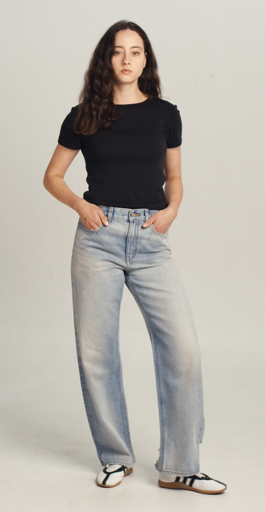 Video of a woman wearing a black wool tee shirt and blue jeans walking into frame, turning to show the tee, then walking out of frame.